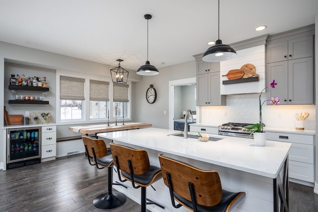 kitchen featuring sink, tasteful backsplash, hanging light fixtures, stainless steel stove, and beverage cooler