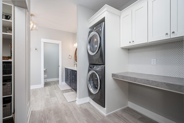 clothes washing area with stacked washer / dryer, a notable chandelier, and light hardwood / wood-style floors