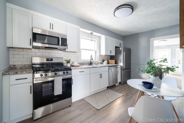 kitchen with stainless steel appliances, sink, light hardwood / wood-style flooring, and white cabinets