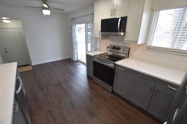 kitchen with dark wood-type flooring, appliances with stainless steel finishes, white cabinetry, light stone counters, and decorative backsplash