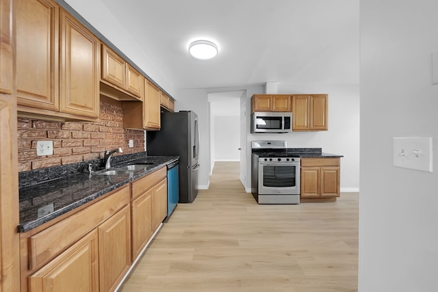 kitchen featuring dark stone countertops, sink, light hardwood / wood-style floors, and appliances with stainless steel finishes