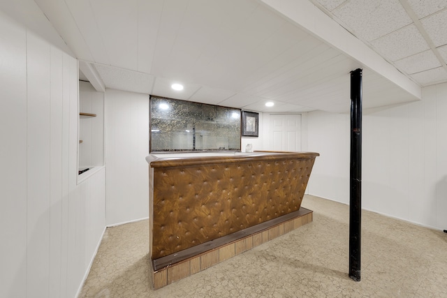 bar featuring light colored carpet, a paneled ceiling, and wood walls