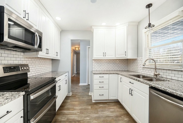 kitchen featuring appliances with stainless steel finishes, pendant lighting, white cabinetry, sink, and hardwood / wood-style flooring