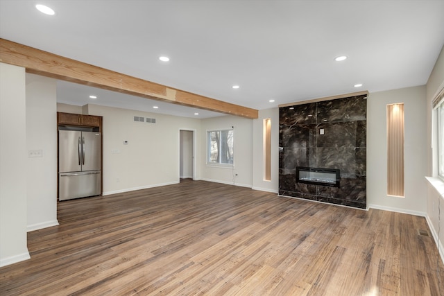 unfurnished living room featuring beamed ceiling, a tiled fireplace, and hardwood / wood-style floors