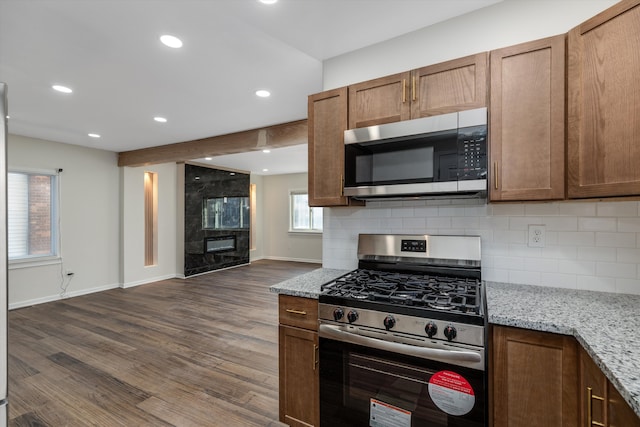 kitchen featuring dark wood-type flooring, light stone counters, stainless steel appliances, a fireplace, and backsplash