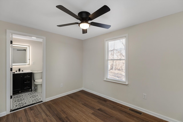 unfurnished bedroom featuring ceiling fan, ensuite bathroom, and dark hardwood / wood-style flooring