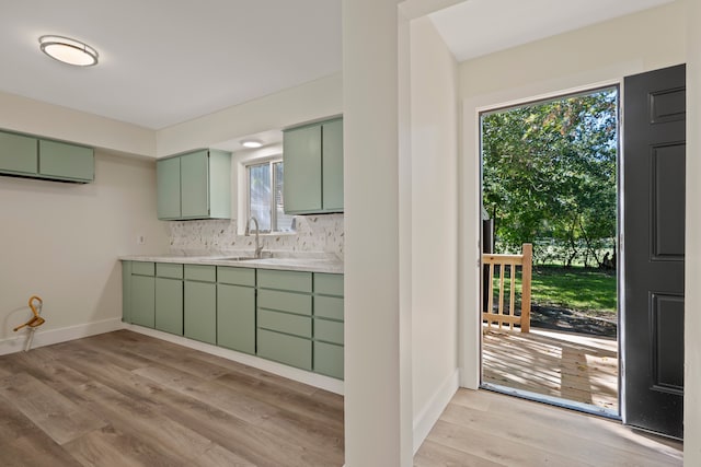 kitchen with backsplash, green cabinetry, sink, and light wood-type flooring