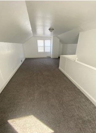 additional living space with vaulted ceiling and dark colored carpet