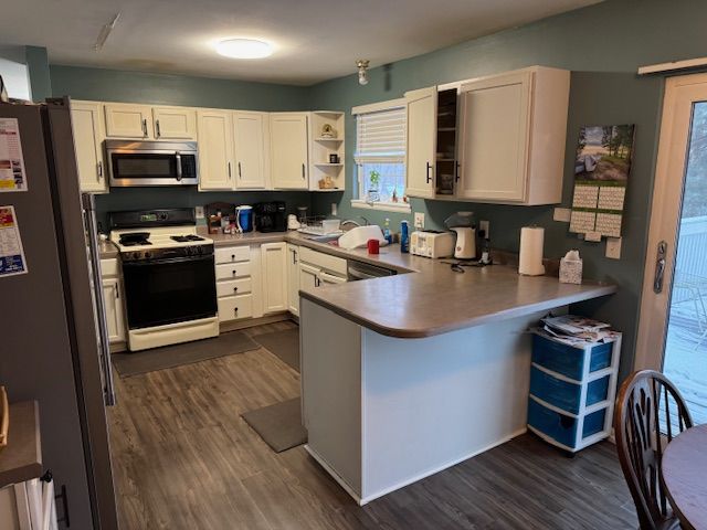 kitchen with dark wood-type flooring, white cabinetry, appliances with stainless steel finishes, and kitchen peninsula