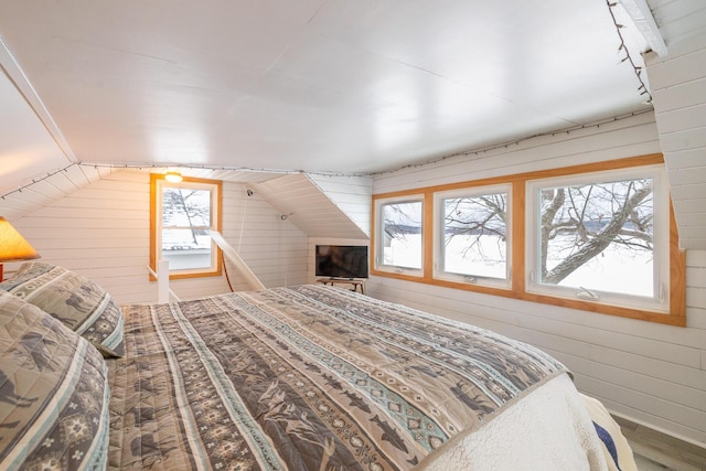 bedroom featuring vaulted ceiling, multiple windows, and wood walls