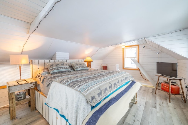 bedroom with wood walls, lofted ceiling, and light wood-type flooring