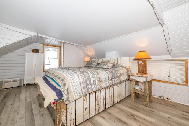 bedroom featuring vaulted ceiling, a wall mounted AC, and light hardwood / wood-style floors