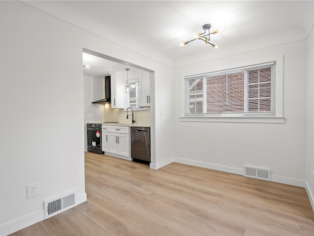 interior space featuring white cabinetry, decorative light fixtures, black electric range, dishwasher, and wall chimney range hood