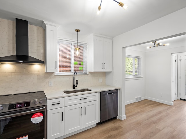 kitchen featuring pendant lighting, sink, white cabinets, stainless steel appliances, and wall chimney range hood