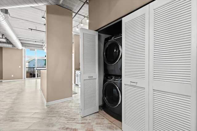 clothes washing area featuring track lighting, stacked washing maching and dryer, and light hardwood / wood-style floors