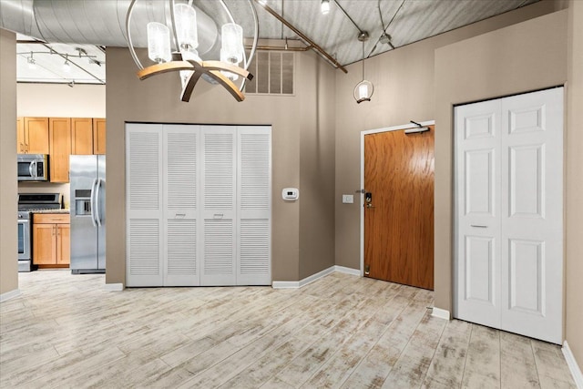 interior space featuring rail lighting, a towering ceiling, light hardwood / wood-style flooring, and stainless steel fridge with ice dispenser