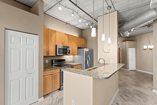 kitchen with sink, hanging light fixtures, appliances with stainless steel finishes, light stone countertops, and a high ceiling