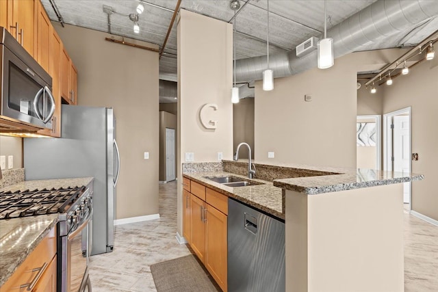 kitchen featuring sink, rail lighting, appliances with stainless steel finishes, light stone counters, and decorative light fixtures