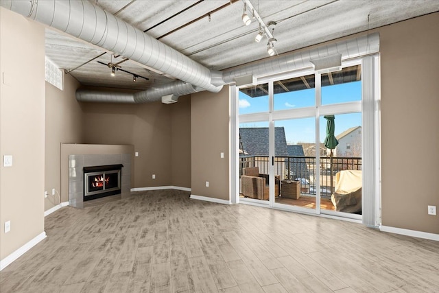 unfurnished living room featuring a wall of windows, rail lighting, a tile fireplace, and light hardwood / wood-style flooring