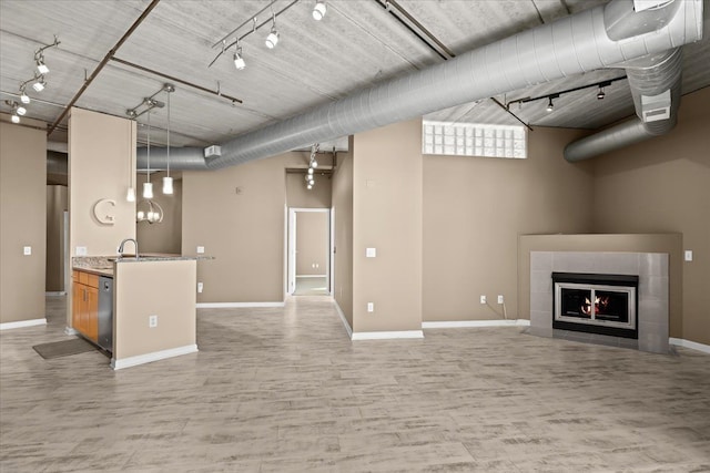 unfurnished living room with a tile fireplace, rail lighting, sink, and light wood-type flooring