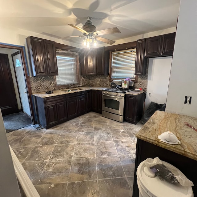 kitchen with stainless steel gas stove, tasteful backsplash, sink, ceiling fan, and light stone counters