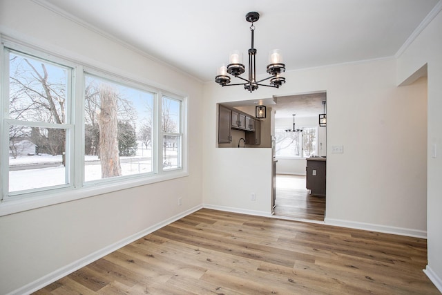 unfurnished dining area with hardwood / wood-style flooring, a healthy amount of sunlight, ornamental molding, and a notable chandelier