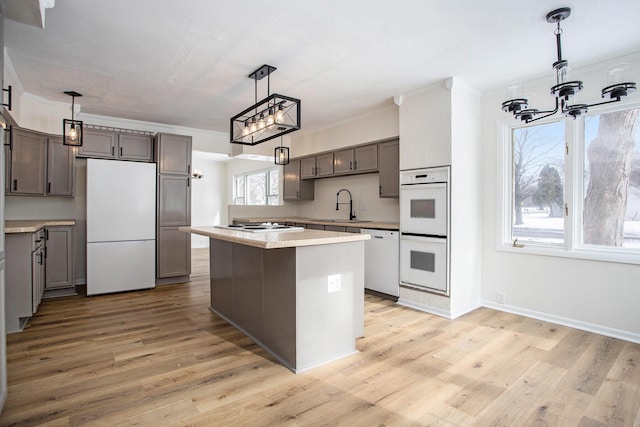 kitchen with pendant lighting, sink, light wood-type flooring, a center island, and white appliances