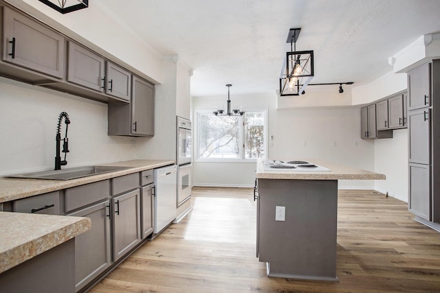 kitchen with pendant lighting, sink, gray cabinetry, a center island, and white appliances