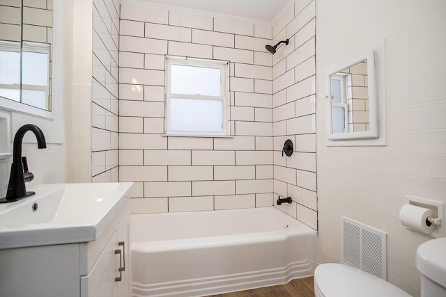 full bathroom featuring toilet, tiled shower / bath, tile walls, vanity, and hardwood / wood-style floors