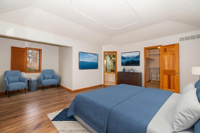 bedroom featuring lofted ceiling, ensuite bath, a textured ceiling, dark hardwood / wood-style flooring, and a walk in closet