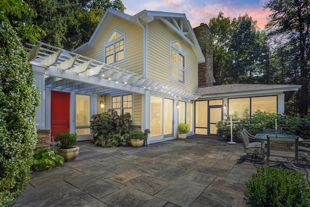 back house at dusk featuring a pergola and a patio