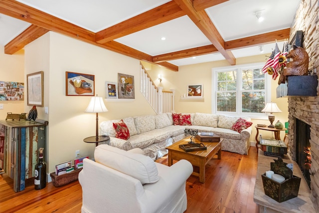 living room featuring wood-type flooring, a stone fireplace, and beam ceiling