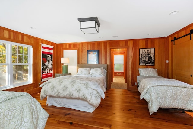 bedroom featuring ornamental molding, a barn door, wood-type flooring, and wooden walls