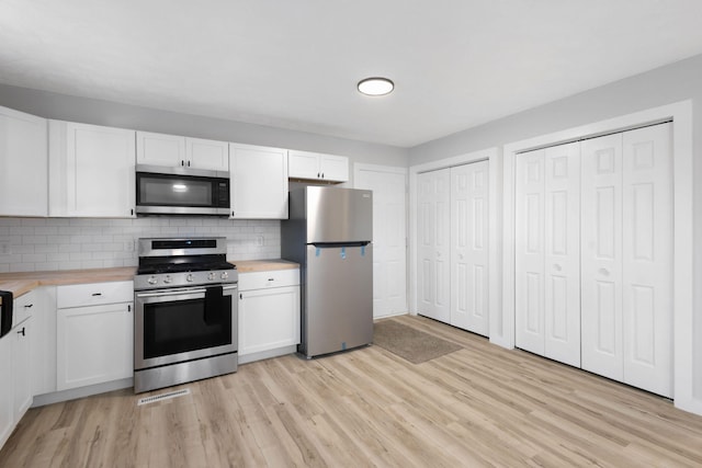 kitchen with appliances with stainless steel finishes, butcher block countertops, white cabinetry, decorative backsplash, and light hardwood / wood-style flooring