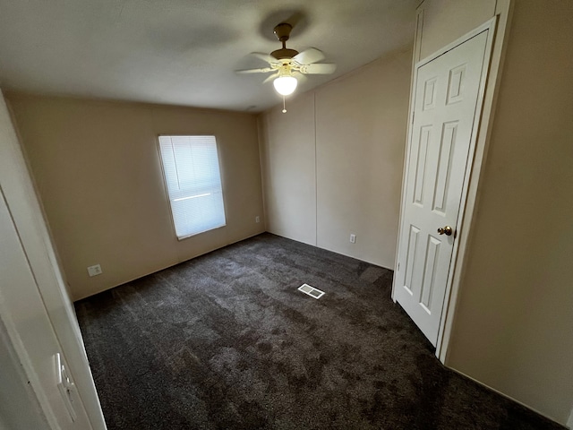 spare room with ceiling fan and dark colored carpet