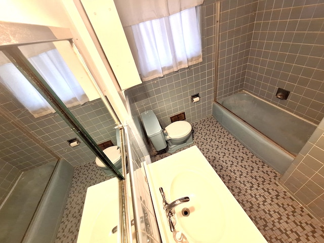 full bathroom with toilet, sink, tile walls, tiled shower / bath combo, and tile patterned flooring