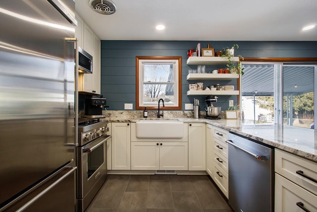 kitchen with high end appliances, sink, white cabinetry, and light stone countertops