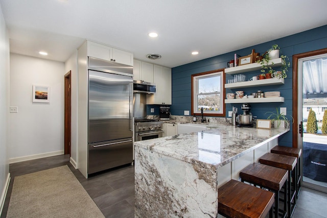 kitchen with high quality appliances, sink, white cabinets, and a breakfast bar