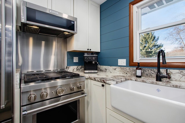 kitchen with sink, wood walls, white cabinetry, light stone counters, and stainless steel appliances