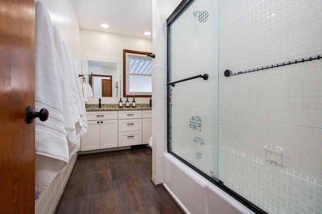 bathroom with wood-type flooring, vanity, and bath / shower combo with glass door