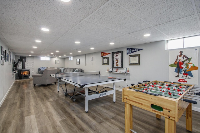 rec room featuring a paneled ceiling, a wood stove, and hardwood / wood-style floors