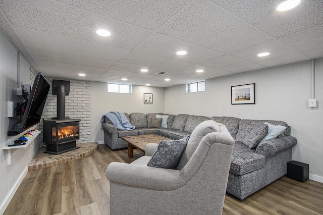 living room with wood-type flooring, a drop ceiling, and a wood stove