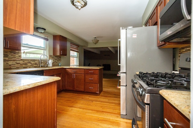 kitchen featuring sink, appliances with stainless steel finishes, kitchen peninsula, light stone countertops, and light hardwood / wood-style floors