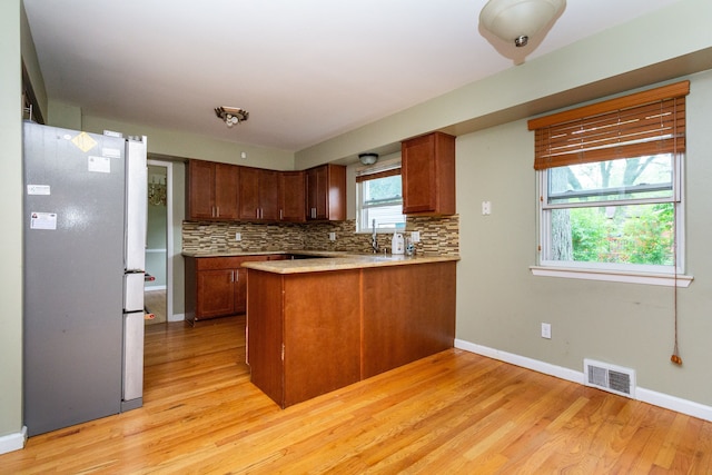 kitchen featuring tasteful backsplash, light hardwood / wood-style floors, stainless steel refrigerator, and kitchen peninsula