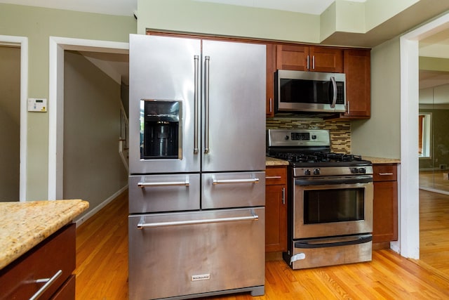 kitchen featuring tasteful backsplash, appliances with stainless steel finishes, light stone countertops, and light hardwood / wood-style flooring