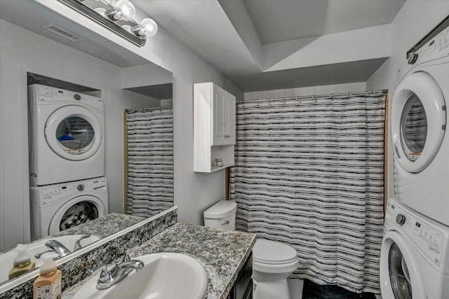 bathroom with vanity, stacked washer and dryer, toilet, and walk in shower