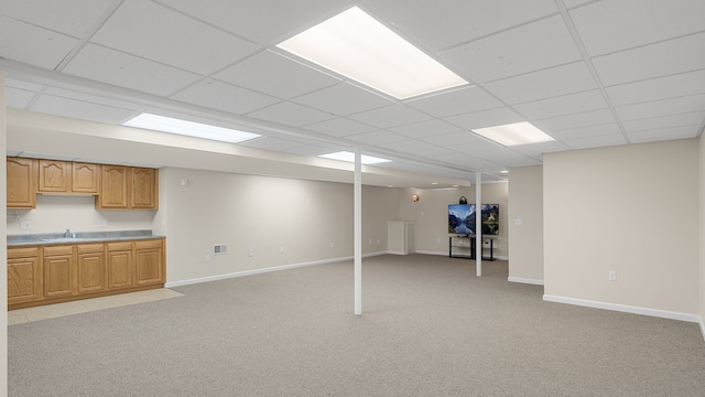 basement featuring a drop ceiling, sink, and light colored carpet