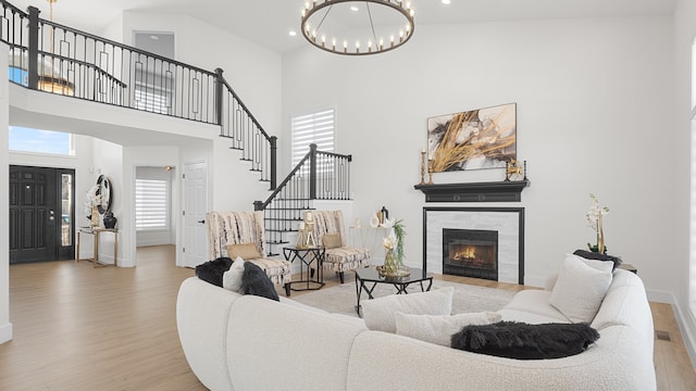 living room featuring an inviting chandelier, light hardwood / wood-style flooring, a tile fireplace, and a high ceiling