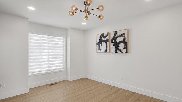 empty room with a chandelier, a wealth of natural light, and light wood-type flooring