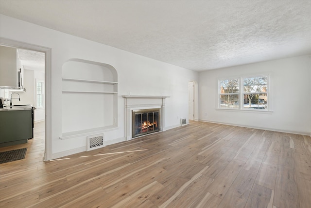 unfurnished living room with built in shelves, sink, light hardwood / wood-style floors, and a textured ceiling